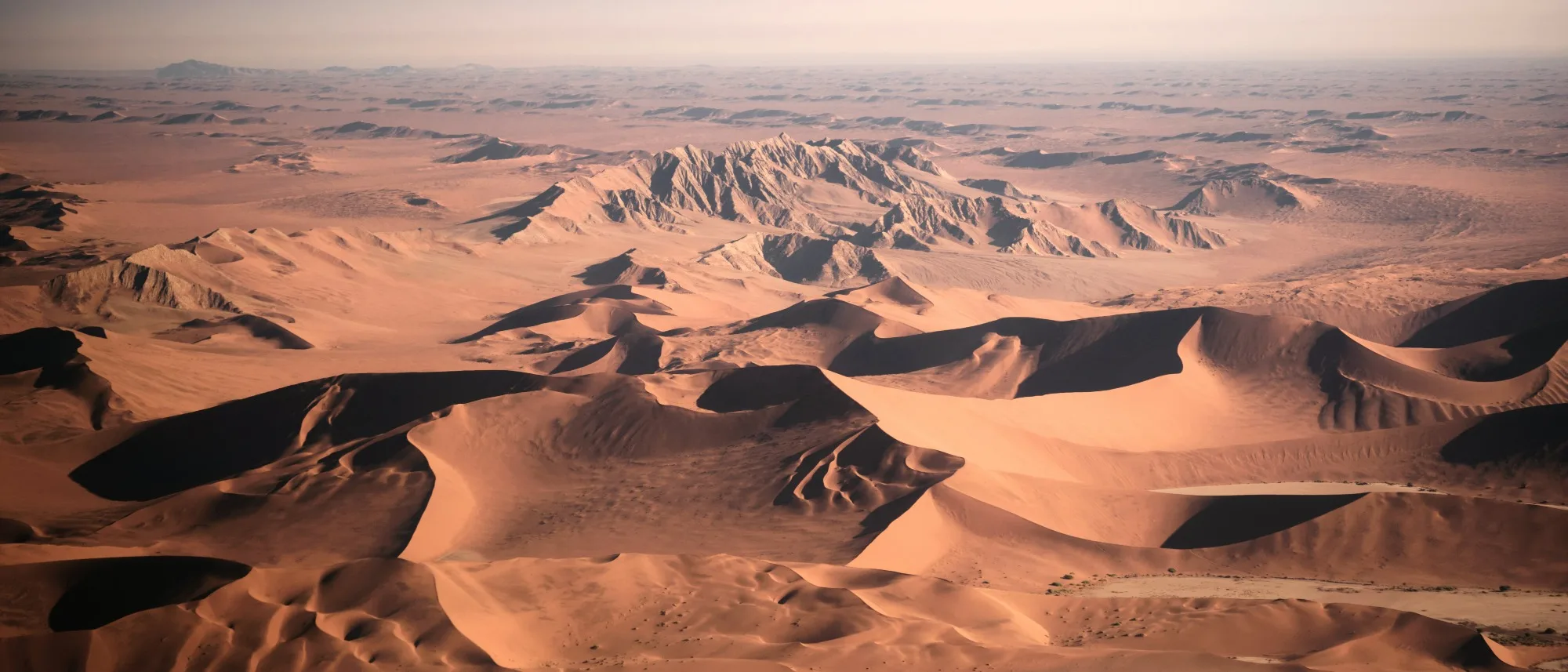 Aerial view of red-orange sand dunes and rocky mountains in Namibia’s Namib Desert